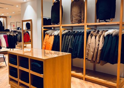 Woolrich shop furniture, view of clothing racks made of oak veneered chipboard
